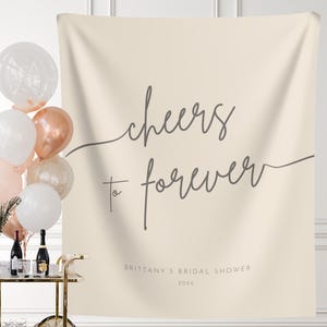 May include: A beige bridal shower backdrop with the text "Cheers to forever" in gray script. The text "Brittany's Bridal Shower 2026" is also included in gray.