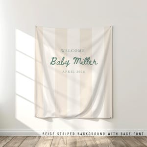 Può includere: Un banner in tessuto a righe beige e bianche con le parole "WELCOME Baby Miller APRIL 2026" in corsivo verde salvia. Lo striscione è appeso a una parete bianca. La parte inferiore dello striscione recita "BEIGE STRIPED BACKGROUND WITH SAGE FONT".