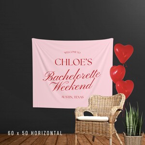 Pu&ograve; includere: Un banner in tessuto rosa con la scritta "WELCOME TO CHLOE'S Bachelorette Weekend AUSTIN, TEXAS" in rosso. Tre palloncini rossi a forma di cuore sono a destra del banner. Una sedia in vimini e una pianta in vaso.