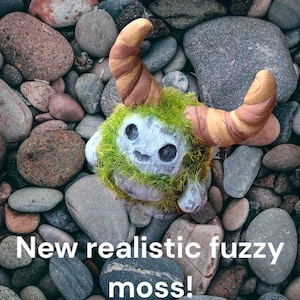 May include: A small, fuzzy, green and brown creature with horns made of clay. The creature is sitting on a bed of small, gray rocks.