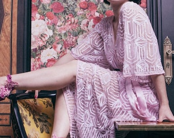 May include: A light purple, patterned robe with a matching belt. The robe is paired with pink high heels adorned with floral embellishments. The background features floral wallpaper and a vintage clock.