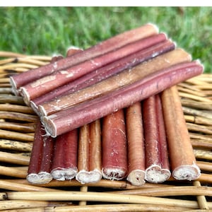 May include: A close-up of a pile of red and brown dog chews. The chews are made of rawhide and are arranged in a neat stack.
