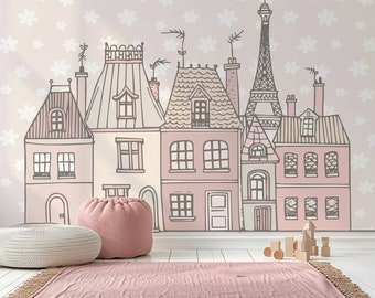May include: A pink and white nursery room with a wall mural of a city skyline. The mural features a pink, white, and gray color scheme and includes a Eiffel Tower. The room also has a pink pouf and a white woven rug.