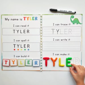以下が含まれることがあります： 「TYLER」と印刷された表紙の開いたワークブック。ワークブックには、名前の読み、スペル、トレース、書き込みのセクションがあります。カラフルなマグネット文字とマーカーも存在します。
