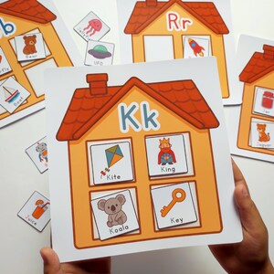 Może przedstawiać: Edukacyjne karty alfabetu z literami i powiązanymi obrazami. Karta 'Kk' przedstawia latawiec, króla, koalę i klucz. Inne karty pokazują niedźwiedzia, motyla i łódź, wspierając wczesną naukę.