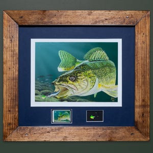 May include: Framed artwork featuring a detailed painting of a fish with its mouth open, capturing a smaller fish. The artwork is set against a dark blue mat and framed in a rustic, light brown wooden frame. Two smaller images are below the main artwork.