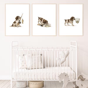 May include: Three framed art prints showing a brown and white puppy fishing. The illustrations depict the puppy with fishing equipment and fish. The prints are displayed above a white cot with pillows and a rocking horse.