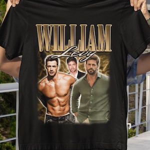 May include: Black t-shirt featuring a gold-colored text that reads "WILLIAM LEVY" above three images of a man. The man is shirtless in one image, and wearing a green shirt in another.