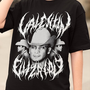 May include: Black t-shirt with a white graphic print of a man wearing a cowboy hat. The graphic includes the text "VALENTINO" and "EL ZETA 03".