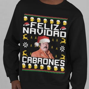 Puede incluir: Sudadera negra con un diseño festivo. El diseño incluye el texto "FELIZ NAVIDAD CABRONES" en blanco, un retrato de un hombre con un gorro de Papá Noel, jarras de cerveza, copos de nieve y renos.