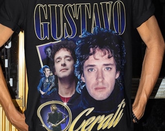 May include: A black t-shirt with a graphic print of a man with the text "Gustavo Cerati" in gold lettering. The man is wearing a blue shirt and has dark hair. The t-shirt has a crew neck and short sleeves.