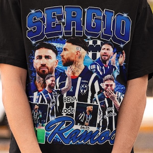 May include: Black t-shirt featuring a graphic of soccer players with the name "SERGIO" in blue and white lettering. The shirt includes the name "Ramos" in a stylized script. The design incorporates images of soccer players.