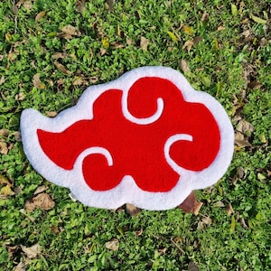 Può includere: Tappeto a forma di nuvola rosso e bianco con una texture soffice. Il tappeto è su una superficie erbosa verde.