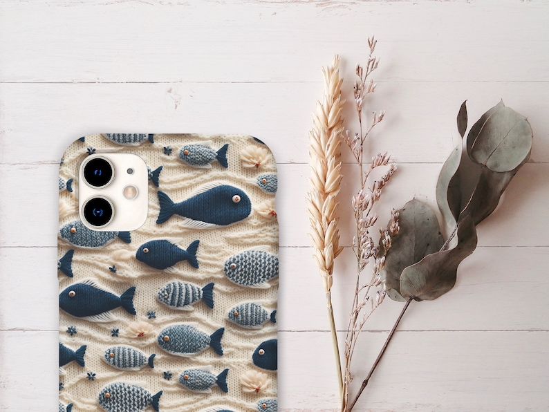 May include: A white phone case featuring a pattern of blue and white fish. The case has a camera lens cutout and a white background.