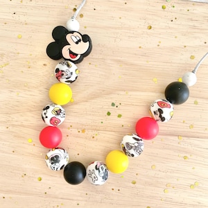 May include: A necklace featuring a black Mickey Mouse head charm and a series of colorful beads. The beads include yellow, red, black, and white with Mickey Mouse designs. The necklace is strung on a gray cord.