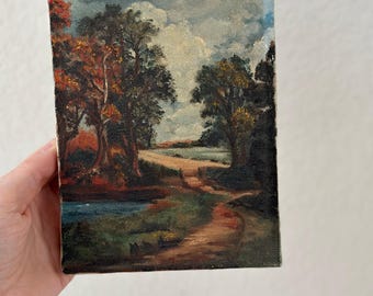 May include: A small oil painting depicting a country road winding through a forest with a stream in the foreground. The trees are painted in shades of green, brown, and red, and the sky is a light blue with white clouds.