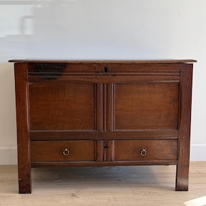Puede incluir: Un cofre de madera antigua de color marrón oscuro con dos cajones y tiradores de anillo. El cofre tiene forma rectangular con una parte superior plana y está sostenido por cuatro patas robustas. La veta de la madera es visible.