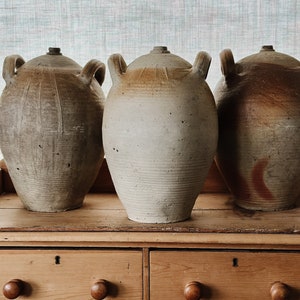May include: Three large, ceramic, glazed jars with handles, in shades of brown and white, sitting on a wooden dresser with two drawers.