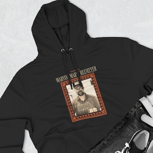 May include: Black hoodie featuring a framed sepia-toned portrait of a man with the text "IN MEMORY OF MARVIN MAR HEEMEYER". The portrait is in a decorative orange frame. The hoodie has a drawstring hood.