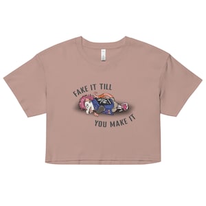 May include: A light pink cropped t-shirt with a graphic of a possum wearing a punk rock outfit and the text "Fake it till you make it".