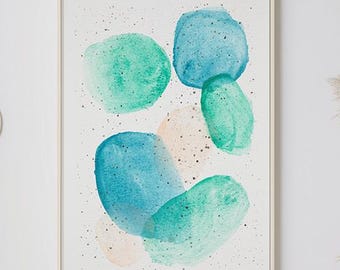 May include: A framed abstract watercolor painting with blue and green shapes on a white background. The painting is hanging on a white wall above a white couch with pillows and a throw blanket.