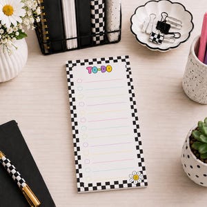 May include: A rectangular to-do list notepad featuring a black and white checkered border, pastel-colored horizontal lines with circular checkboxes, the text TO-DO in colorful bubble letters, and a small smiling daisy graphic at the bottom.