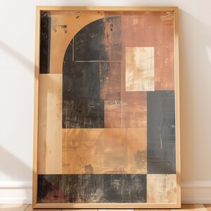 May include: Abstract art print in a wooden frame. The artwork features geometric shapes in shades of brown, black, and beige. The composition includes a semi-circle, rectangles, and squares, creating a modern aesthetic. The framed art is leaning against a white wall.
