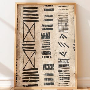 May include: Abstract art print in a wooden frame. The artwork features vertical bands of black geometric shapes and lines on a beige background. The print is displayed against a white wall and wooden floor.