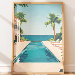 May include: A framed art print depicts a serene poolside scene. The artwork features a turquoise pool, palm trees, and lounge chairs, with a building on the left and the ocean in the background. The print is encased in a light brown wooden frame.