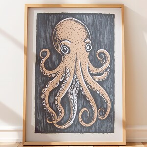 May include: A framed wall art print featuring a tan octopus illustration with dark outlines and visible suction cups on its tentacles. The octopus is set against a dark charcoal gray background with vertical white etched lines, all enclosed in a light wood frame.