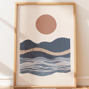 May include: Abstract landscape art print in a wooden frame. The artwork features a large brown circle above dark blue mountain shapes and wavy lines, with a light beige background. A gold-colored band runs across the middle of the image.