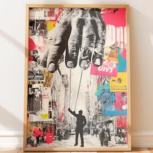 Puede incluir: Impresión artística enmarcada que presenta una gran mano en escala de grises sobre una escena de calle urbana. Una figura silueteada sostiene cuerdas unidas a la mano. El fondo es un collage de carteles coloridos y salpicaduras de pintura.