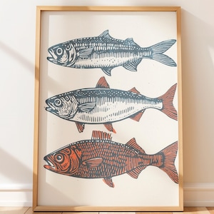 Puede incluir: Un grabado enmarcado con tres ilustraciones estilizadas de peces. Los peces están representados en tonos azules, blancos y naranjas, con detalles de líneas. La obra de arte está enmarcada en un marco de madera natural, ideal para decoración náutica.