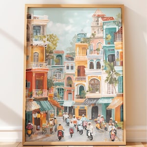 Op de afbeelding: Een ingelijste kunstdruk die een levendige straatscène toont met kleurrijke gebouwen in tinten van oranje, blauwgroen en roze. Scooters en mensen bevinden zich op straat. Het kunstwerk zit in een houten lijst.