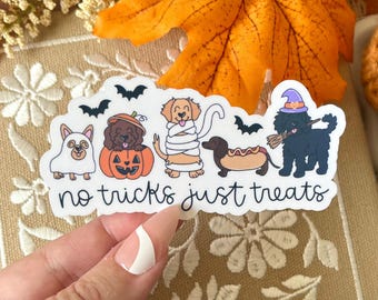 May include: A white die-cut sticker featuring five dogs in Halloween costumes, including a ghost, a pumpkin, a mummy, a hot dog, and a witch with a broom, alongside black bats and the text "no tricks just treats" in a black cursive font.