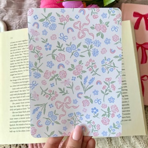 May include: A white card with a floral pattern in shades of pink, blue, and green. The pattern includes small flowers, bows, and rainbows.