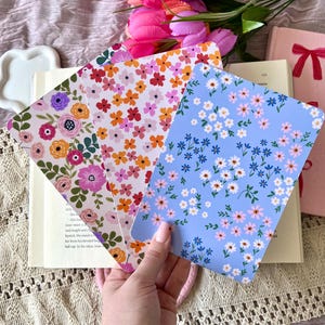 May include: Three floral patterned bookmarks, one with pink and orange flowers on a white background, one with purple and orange flowers on a white background, and one with pink and blue flowers on a light blue background.