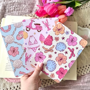 May include: Three patterned cards with a summer theme. One card has a light blue background with seashells and hibiscus flowers. Another card has a pink scooter, bikini, and lobster. The third card has flowers, seashells, and bows.