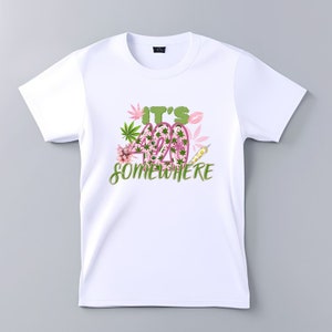 Op de afbeelding: Wit T-shirt met een roze en groene afbeelding met de tekst "It's 420 Somewhere".