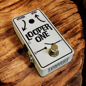 May include: White guitar pedal with black text that reads "Looper One" and "Tomriff Custom". The pedal has a knob, two switches, and an input and output jack.