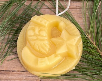 May include: A yellow beeswax ornament shaped like a Santa Claus holding a star. The ornament has a white string for hanging.