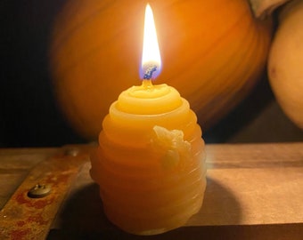 May include: A lit beeswax candle shaped like a honeycomb with a small bee design. The candle is sitting on a wooden surface with a pumpkin in the background.