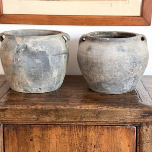 May include: Two gray ceramic pots with handles on a wooden table. The pots are weathered and have a rustic look.