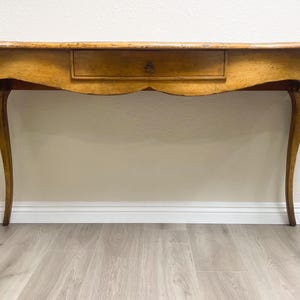 May include: A light wood console table with a single drawer and curved legs. The table has a light wood finish and a simple design.