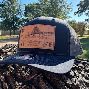 Könnte beinhalten: Eine dunkelblaue und graue Trucker-Kappe mit einem braunen Leder-Patch, auf dem ein Bild der Golden Gate Bridge, der Text "Dead & Company, San Francisco, CA July 14-16, 2023" und vier tanzende Bären abgebildet sind.