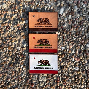 May include: Three rectangular patches featuring the California Republic flag. Two patches are tan with a brown bear, red stripe, and the text "CALIFORNIA REPUBLIC." The third patch is white with the same design.