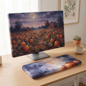 Könnte beinhalten: Eine Computermonitorabdeckung und eine passende Tastatur-Handballenauflage mit einem Druckmotiv eines Kürbisfeldes bei Nacht unter einem Vollmond, mit roten Scheunen im Hintergrund, dunklen violetten Wolken und orangefarbenen Kürbissen.