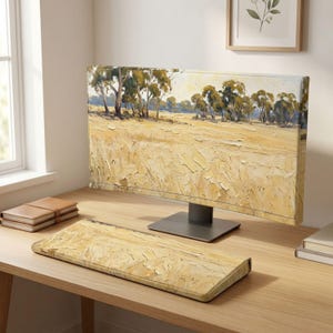 Könnte beinhalten: Ein Computermonitor und eine passende rechteckige Tastatur-Handballenauflage, beide mit einem texturierten Ölgemälde-Druck eines goldenen Weizenfeldes unter einem hellen Himmel mit Bäumen. Der Monitor steht auf einem dunkelgrauen Fuß.