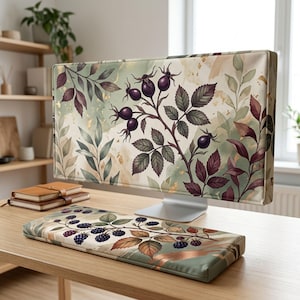 Puede incluir: Una funda para monitor de computadora y un reposamuñecas para teclado a juego con un estampado botánico de bayas de color púrpura oscuro y hojas sobre un fondo verde salvia y crema con detalles dorados. El conjunto muestra un patrón natural.
