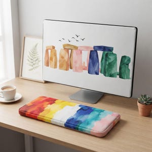 Könnte beinhalten: Eine rechteckige Tastatur-Handballenauflage mit einem lebendigen, mehrfarbigen Aquarell-Verlaufsmuster in Rot-, Orange-, Gelb-, Weiß-, Blau- und Rosatönen. Die Oberfläche hat eine glatte, stoffartige Textur mit abgerundeten Kanten und Ecken.